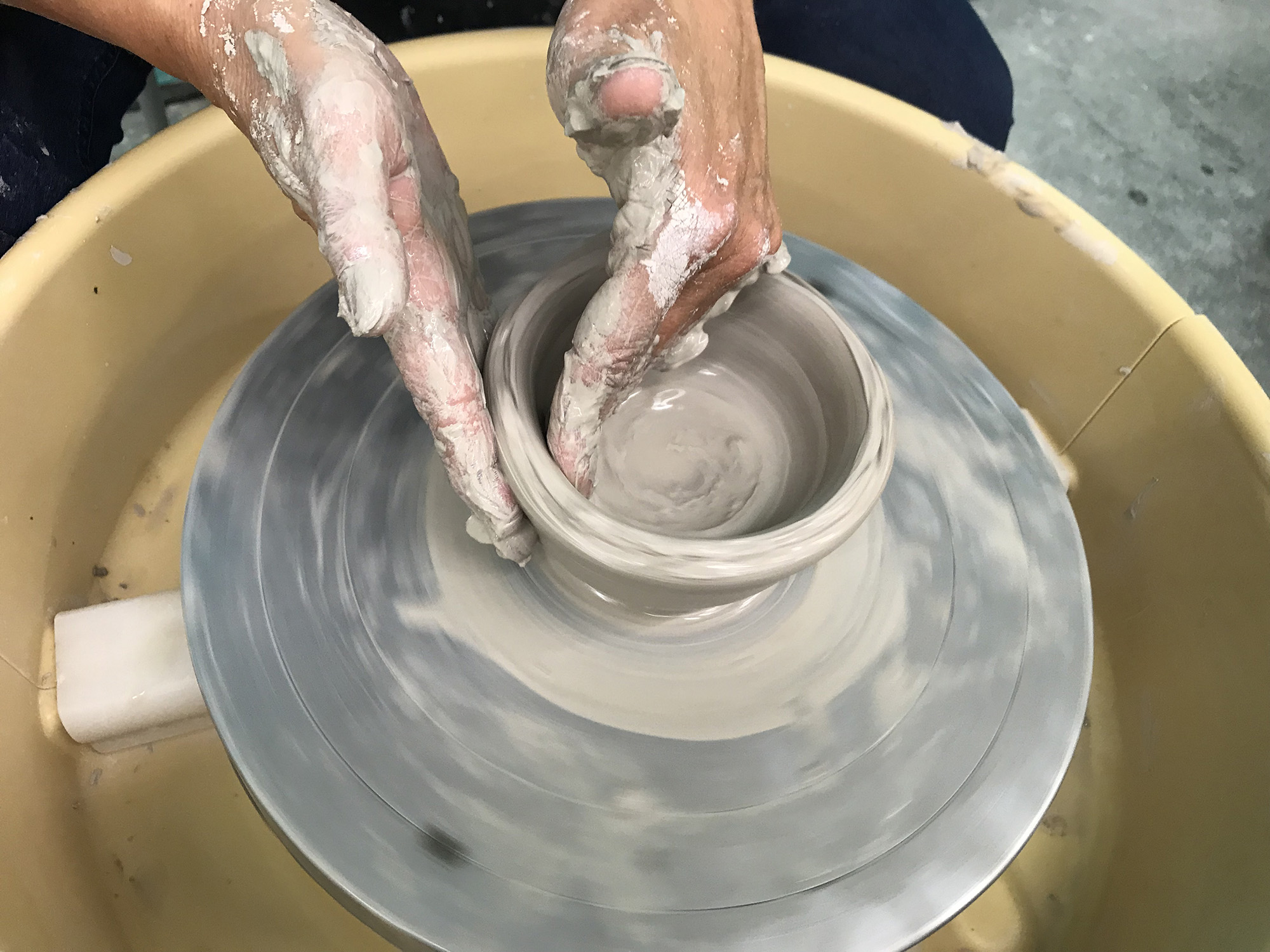 A student making a clay bowl on the wheel.